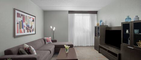 A modern living room with a sectional sofa, a coffee table, a flat-screen TV, and a cabinet with decorative items.