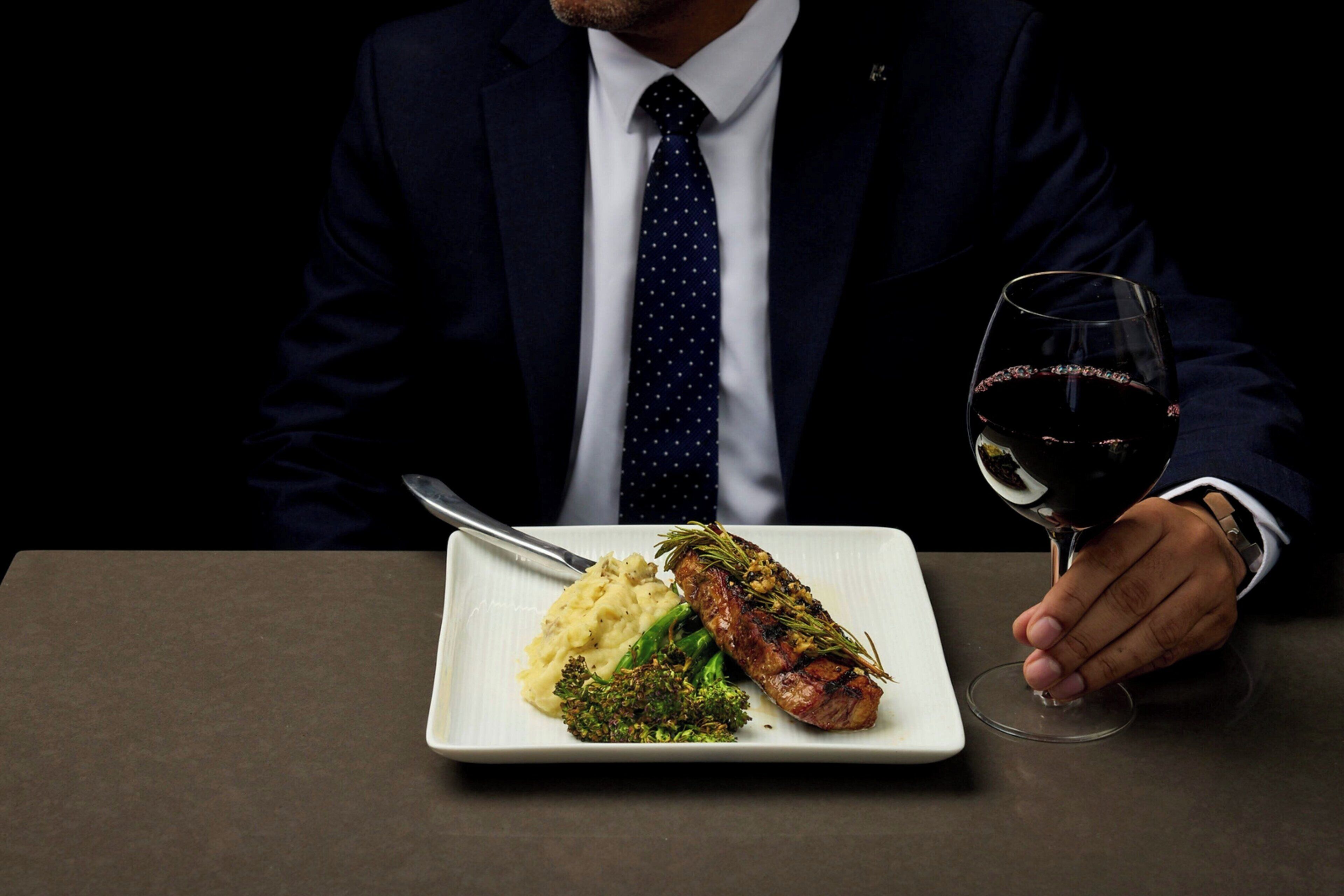 A person seated at a table with a plate of food and a wine glass.