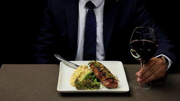 A person seated at a table with a plate of food and a wine glass.