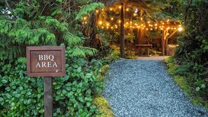 A sign indicating a BBQ area, surrounded by greenery and string lights. - Middle Beach Lodge (Tofino)