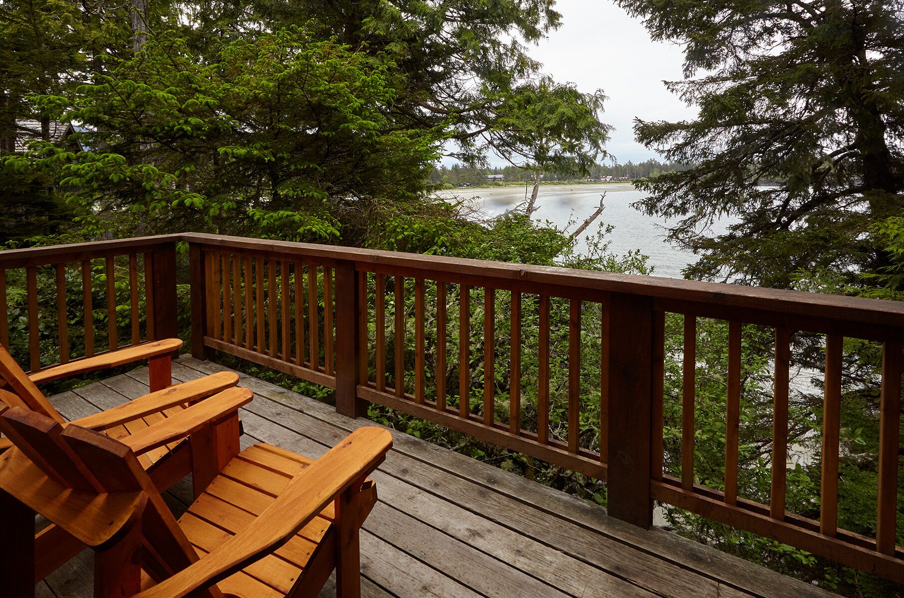 A wooden deck with a railing overlooking a body of water, surrounded by trees.