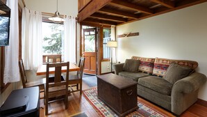 A cozy living room with a wooden ceiling, a sofa with patterned cushions, a wooden coffee table, and a dining area with a table and chairs. - Middle Beach Lodge (Tofino)