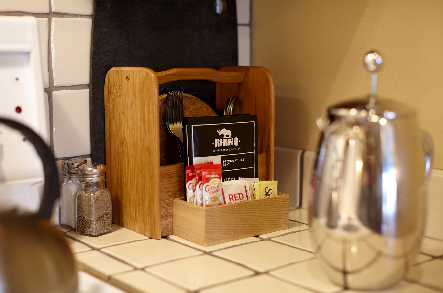 A kitchen counter with a coffee maker, a wooden box containing coffee beans and a coffee menu, and salt and pepper shakers.
