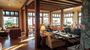 A spacious living room with wooden beams, large windows, and a stone wall. - Middle Beach Lodge (Tofino)