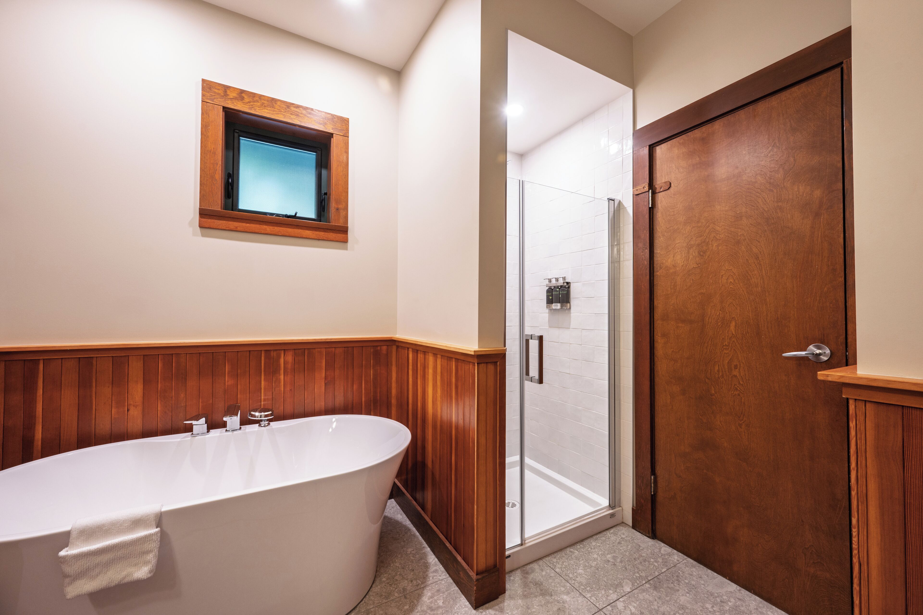 A bathroom with a freestanding bathtub, a glass shower enclosure, and a wooden door.