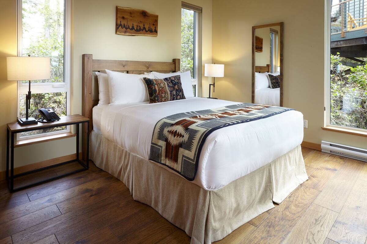 A neatly made bed with a patterned blanket, a bedside lamp, and a nightstand with a phone.