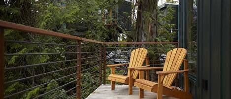 Une terrasse en bois avec deux fauteuils Adirondack, entourée d’une rambarde en métal et d’une végétation luxuriante.