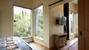 A bedroom with large windows, a bed, a wooden cabinet, and a TV. - Middle Beach Lodge (Tofino)
