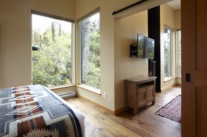 A bedroom with large windows, a bed, a wooden cabinet, and a TV.