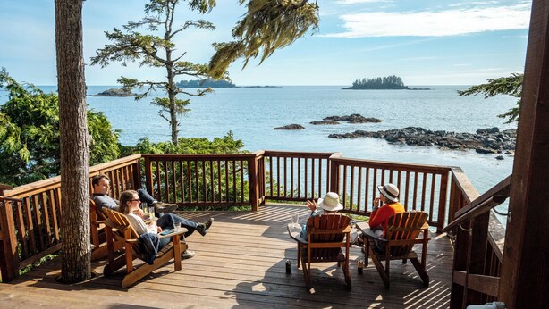 A wooden deck with outdoor seating, overlooking a body of water with rocky outcrops and distant land. - Middle Beach Lodge (Tofino)