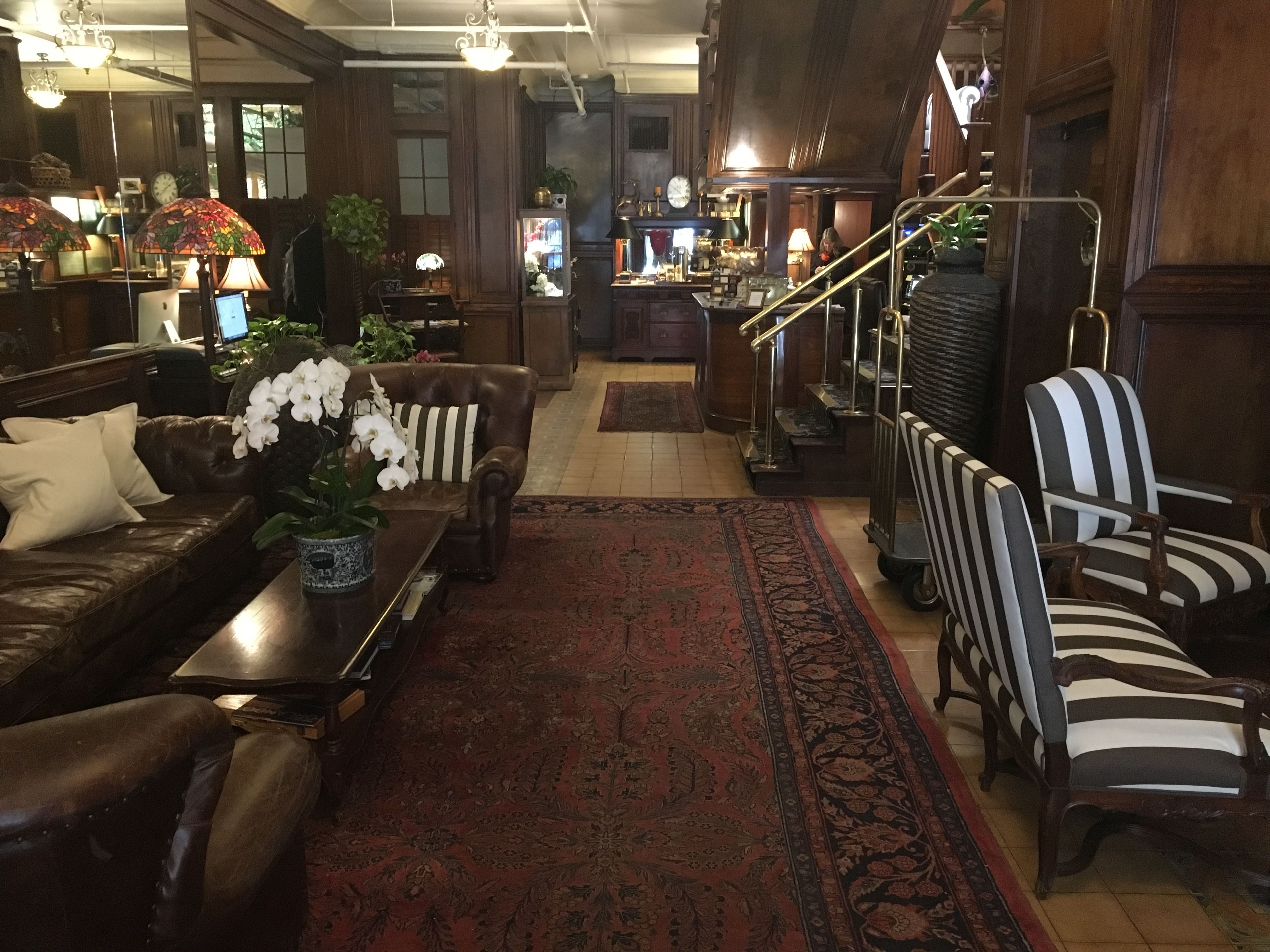 Un hall d’entrée spacieux, doté de canapés en cuir, de fauteuils à rayures, d’un tapis à motifs rouges et d’un escalier avec une rampe.