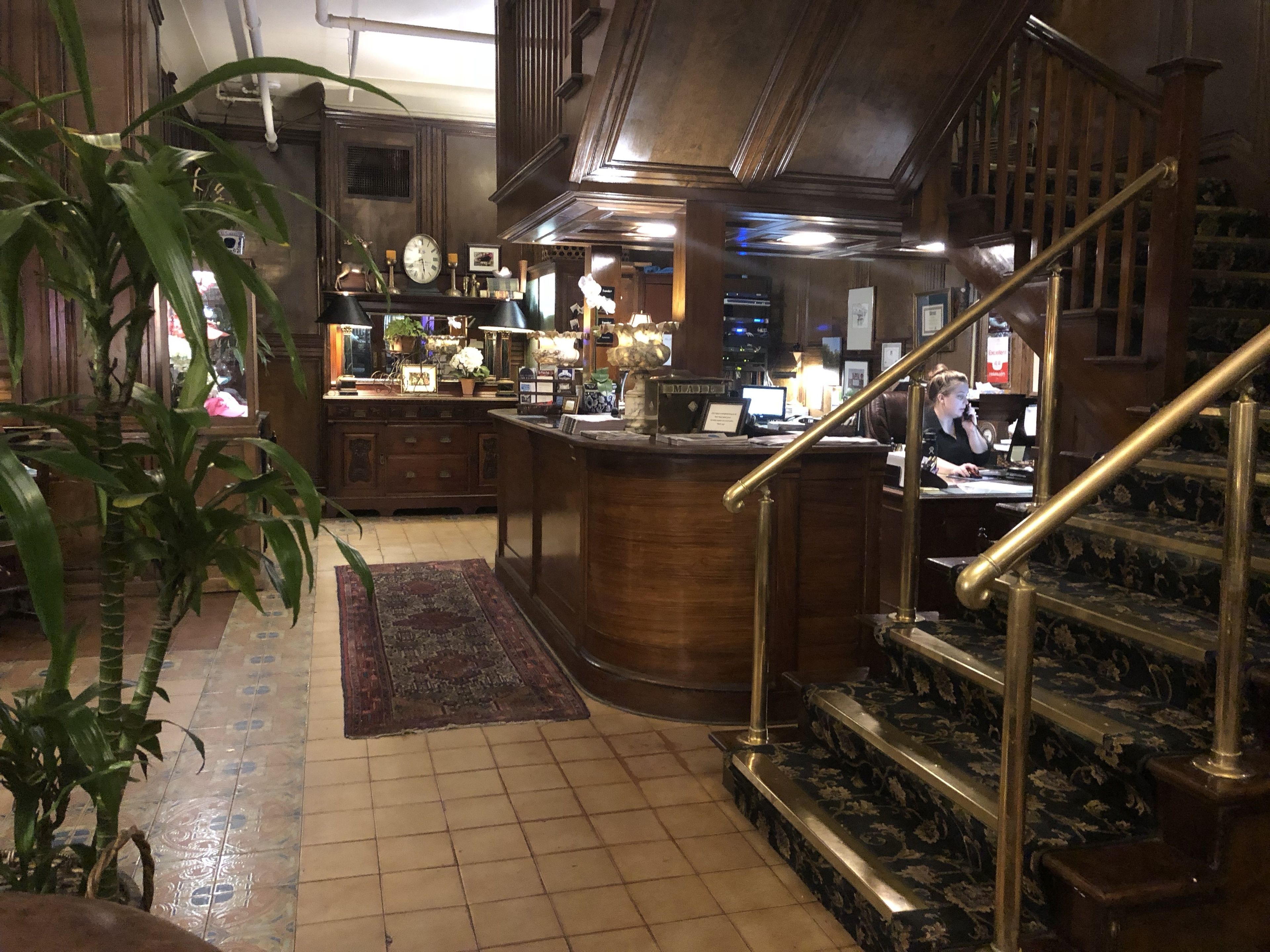 A spacious lobby with a wooden staircase, a reception desk, and a large plant.