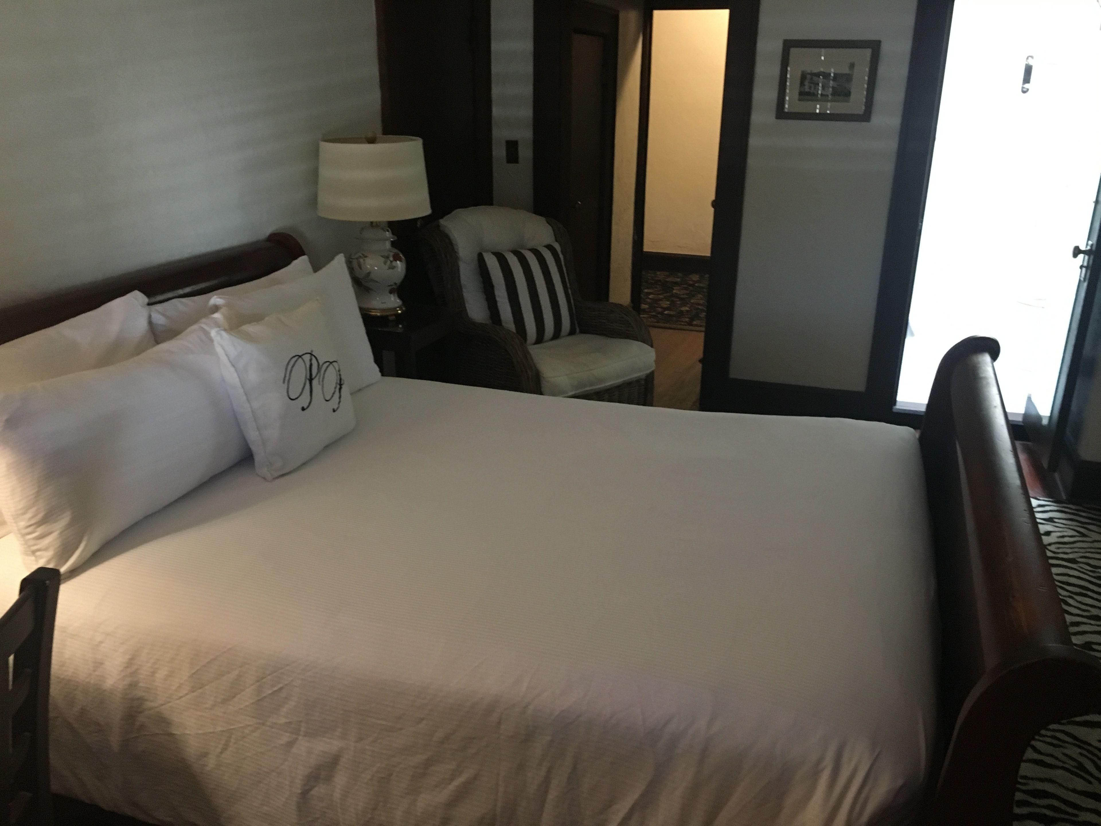 Ein Hotelzimmer mit einem großen Bett, einem Sessel, einer Lampe und einer Tür zu einem anderen Raum.