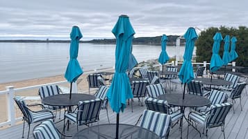 A deck with round tables and striped chairs, overlooking a body of water.