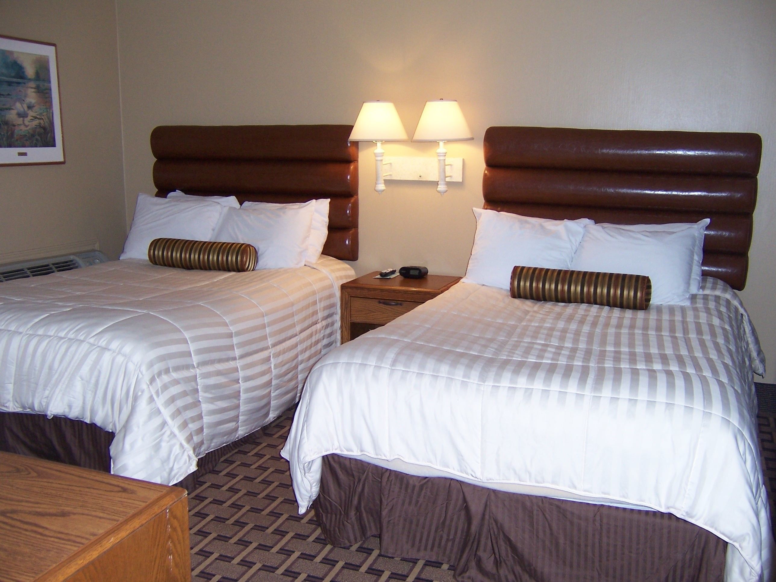 A hotel room with two beds, each with a headboard, a nightstand, and two wall-mounted lamps.