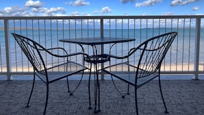 A balcony with a table and two chairs, overlooking a body of water and a distant shoreline. - Pinestead Reef Resort (Traverse City)