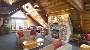A cozy loft-style living room with a stone fireplace, wooden beams, and a large window. - Pinestead Reef Resort (Traverse City)