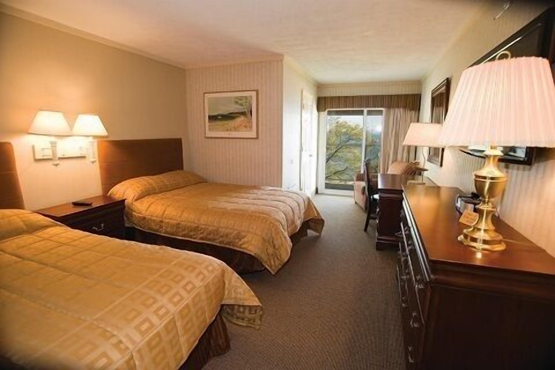 A hotel room with two beds, a desk, a lamp, and a painting on the wall.
