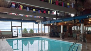 An indoor swimming pool with stone pillars, a view of the sea, and a bar area with chairs. - Pinestead Reef Resort (Traverse City)