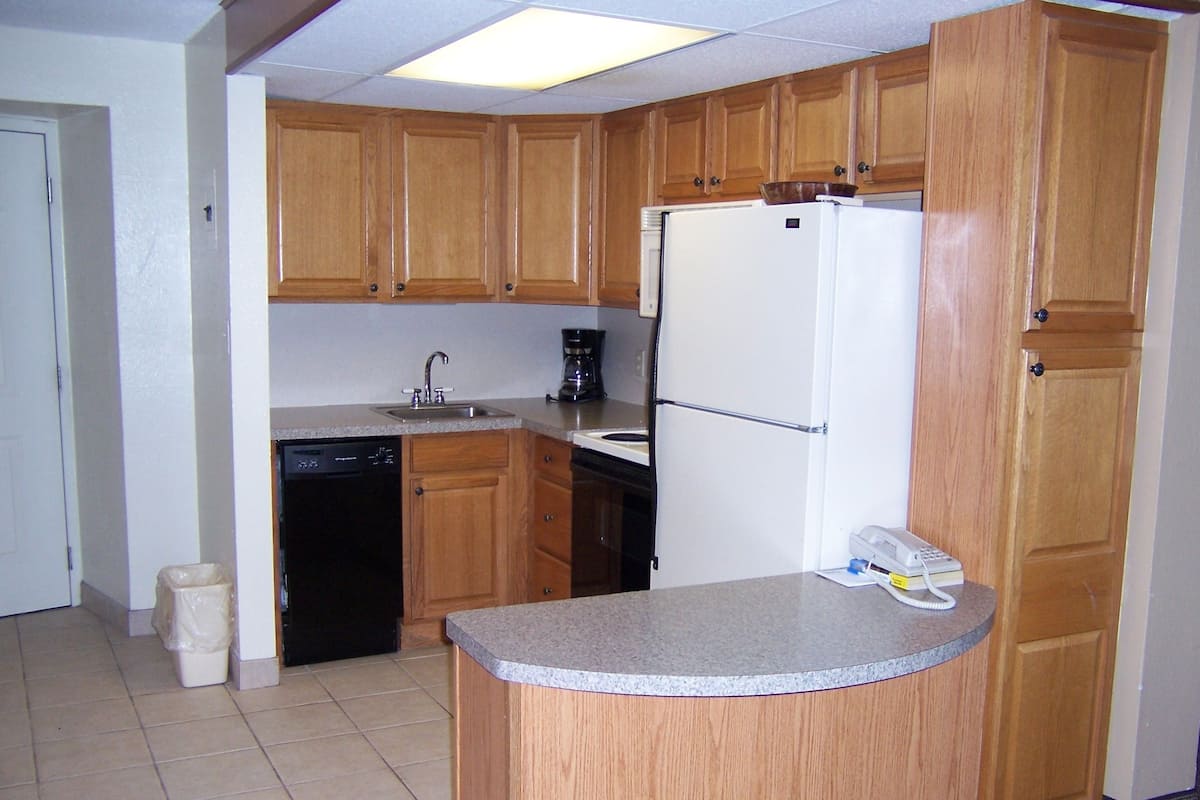 A compact kitchen with wooden cabinets, a built-in dishwasher, a refrigerator, and a small countertop.