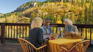 Three people seated at a table with a yellow tablecloth, overlooking a mountainous landscape with autumn foliage. - Spearfish Canyon Lodge (Lead)