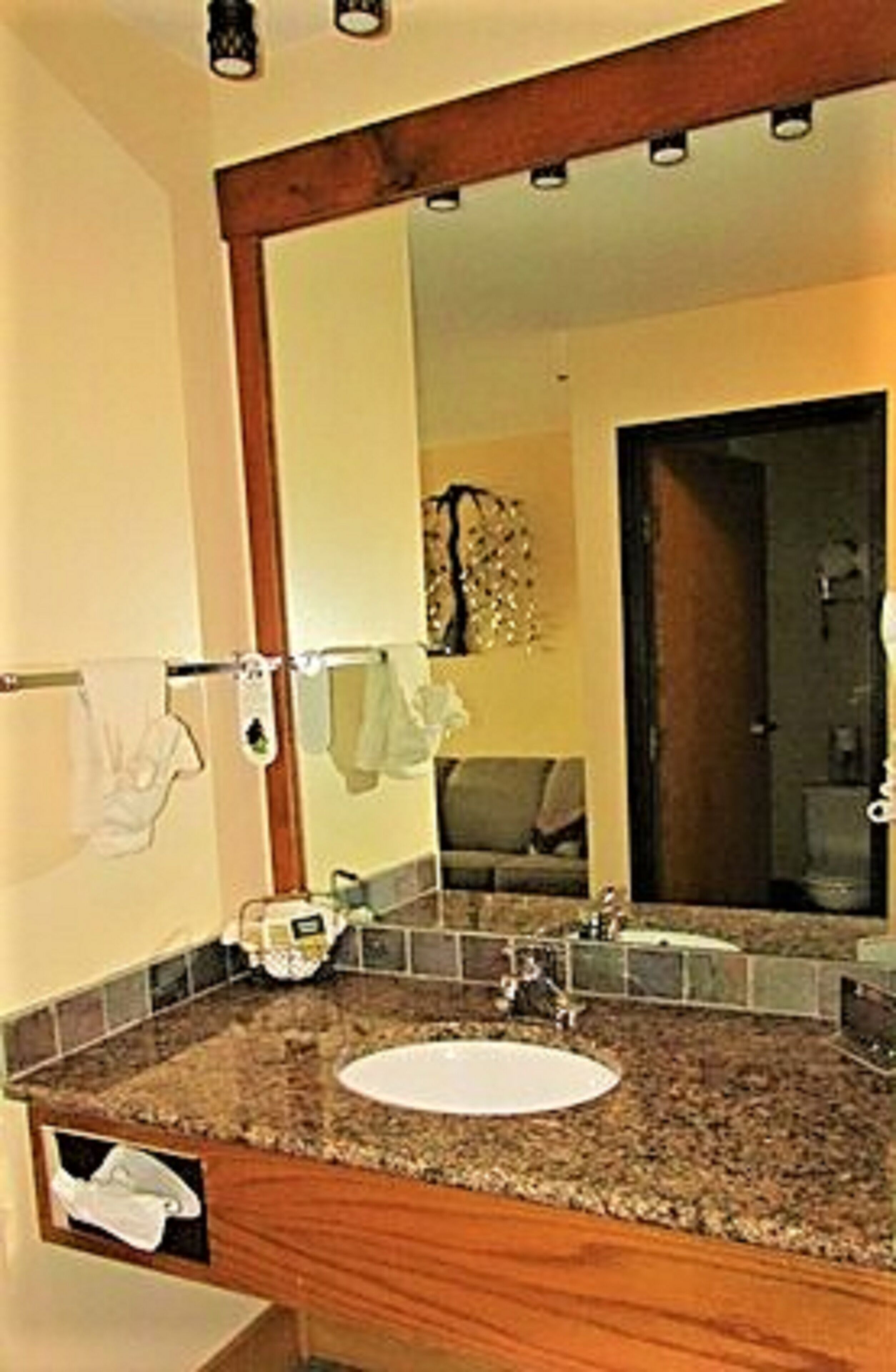 A bathroom with a granite countertop, a white sink, a towel rack, and a large mirror.