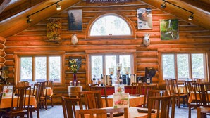 A log cabin-style inn with wooden walls and a high ceiling. There are multiple dining tables and chairs arranged for guests. - Spearfish Canyon Lodge (Lead)