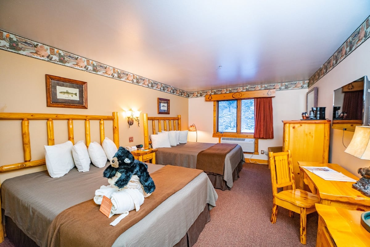 Habitación de hotel con dos camas, cabecero de madera, escritorio con silla, ventana con vistas a árboles y un cuadro en la pared.
