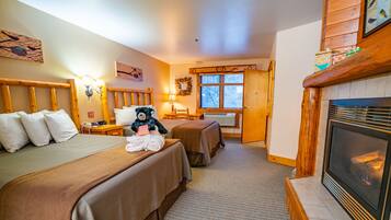 A hotel room with two beds, a fireplace, a window, and a wooden headboard.