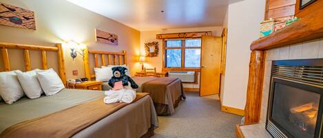 A hotel room with two beds, a fireplace, a window, and a wooden headboard.