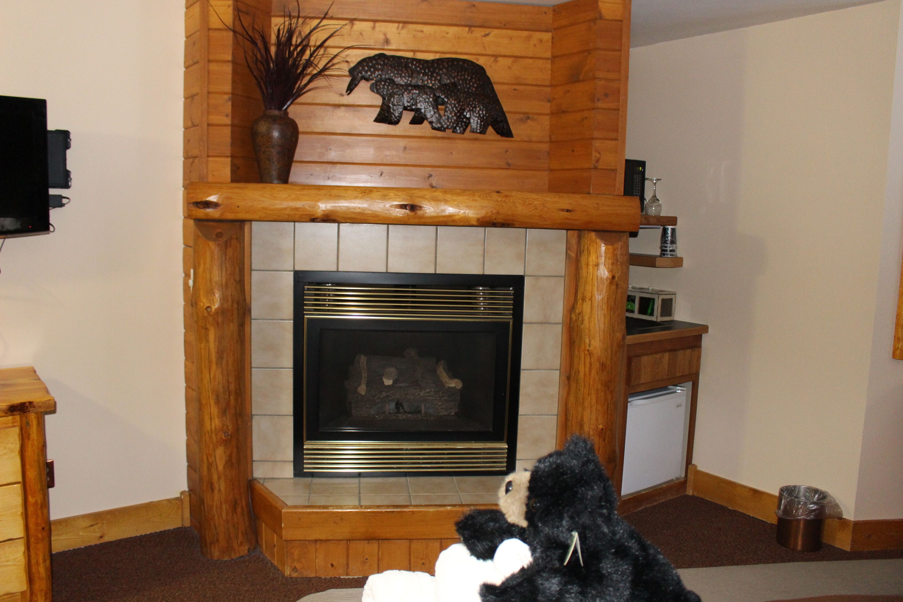 A living room with a fireplace, wooden mantel, and a bear decoration.
