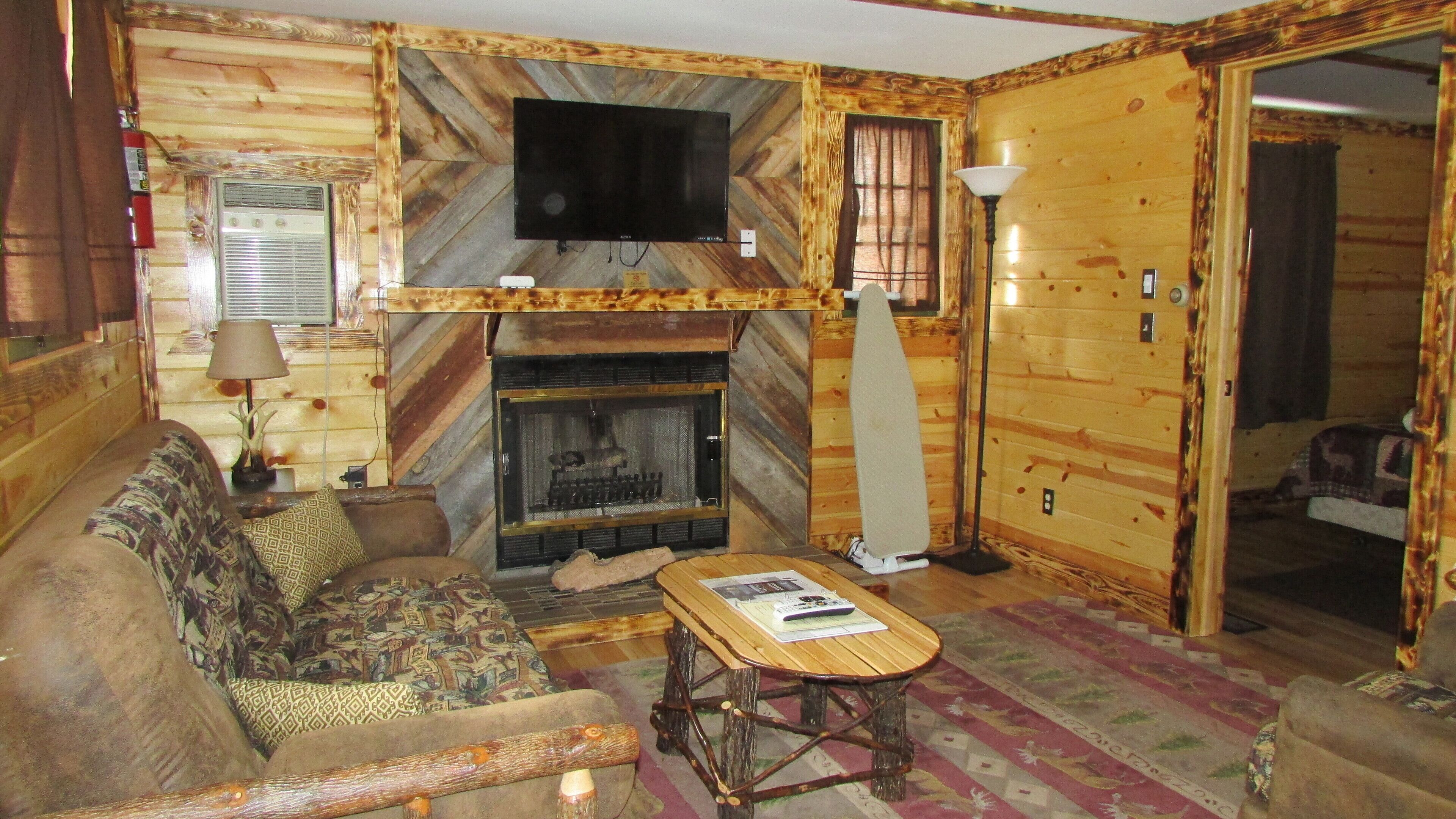 A cozy cabin interior with a fireplace, a television mounted on a wooden wall, a sofa, and a coffee table.