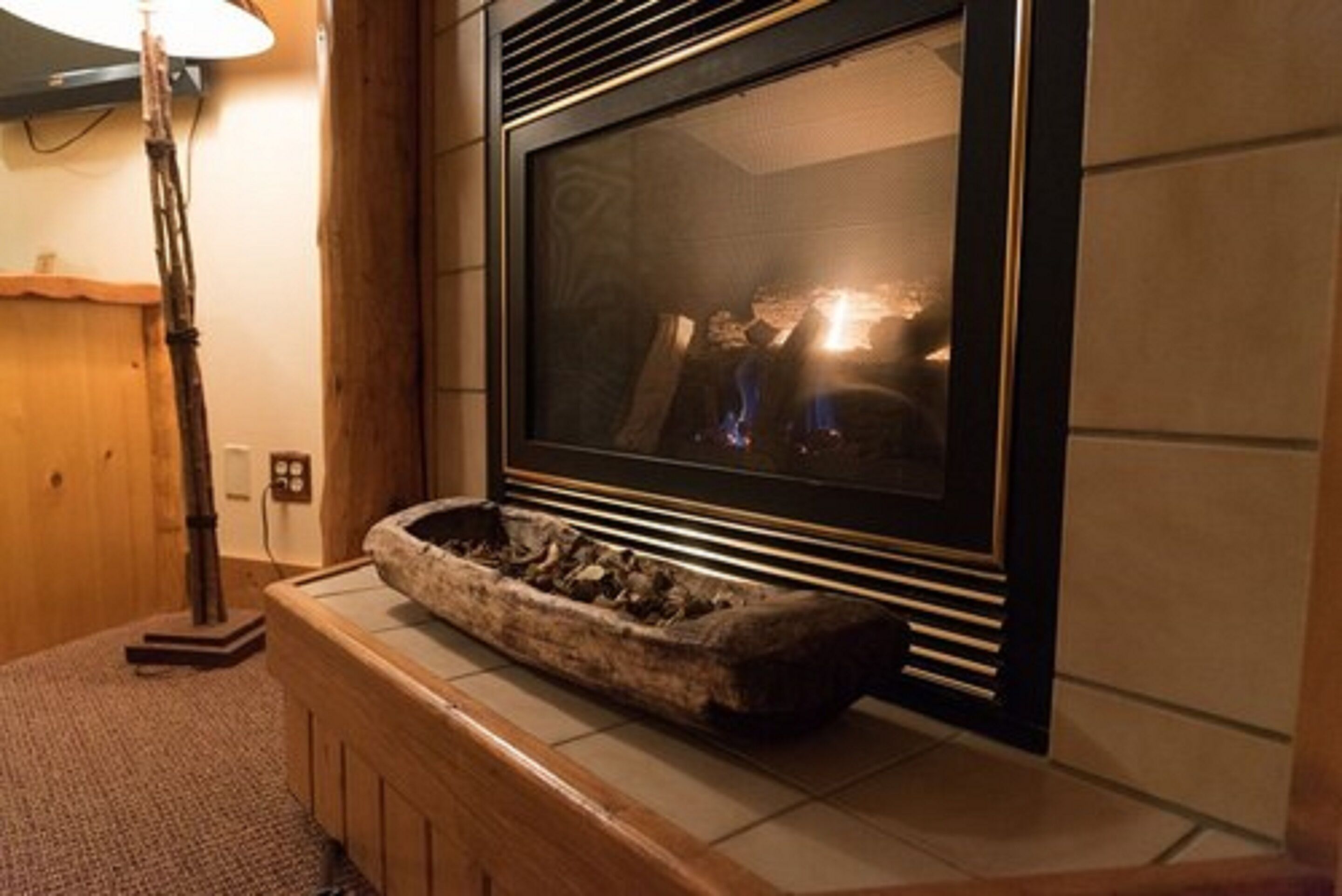 A fireplace with a stone basin, a standing lamp, and a tiled wall.