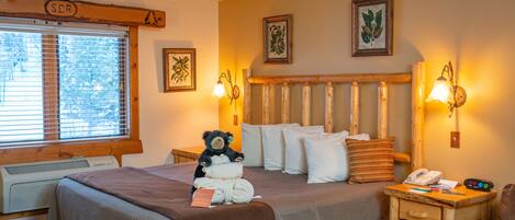A hotel room with a large bed, a bedside table with a lamp, a chair, and a window with blinds.