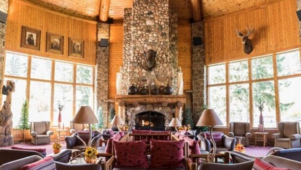 A cozy living room with leather sofas, a central coffee table, and a stone fireplace. - Spearfish Canyon Lodge (Lead)