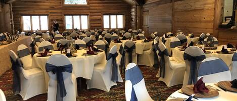 Une salle de banquet avec des tables rondes, des rubans de chaise blancs et bleus, et un décor intérieur en bois.