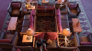 A spacious lounge area with multiple seating options, including sofas and armchairs, arranged around a central coffee table. There are several lamps providing lighting, and the floor is covered with patterned rugs. - Spearfish Canyon Lodge (Lead)