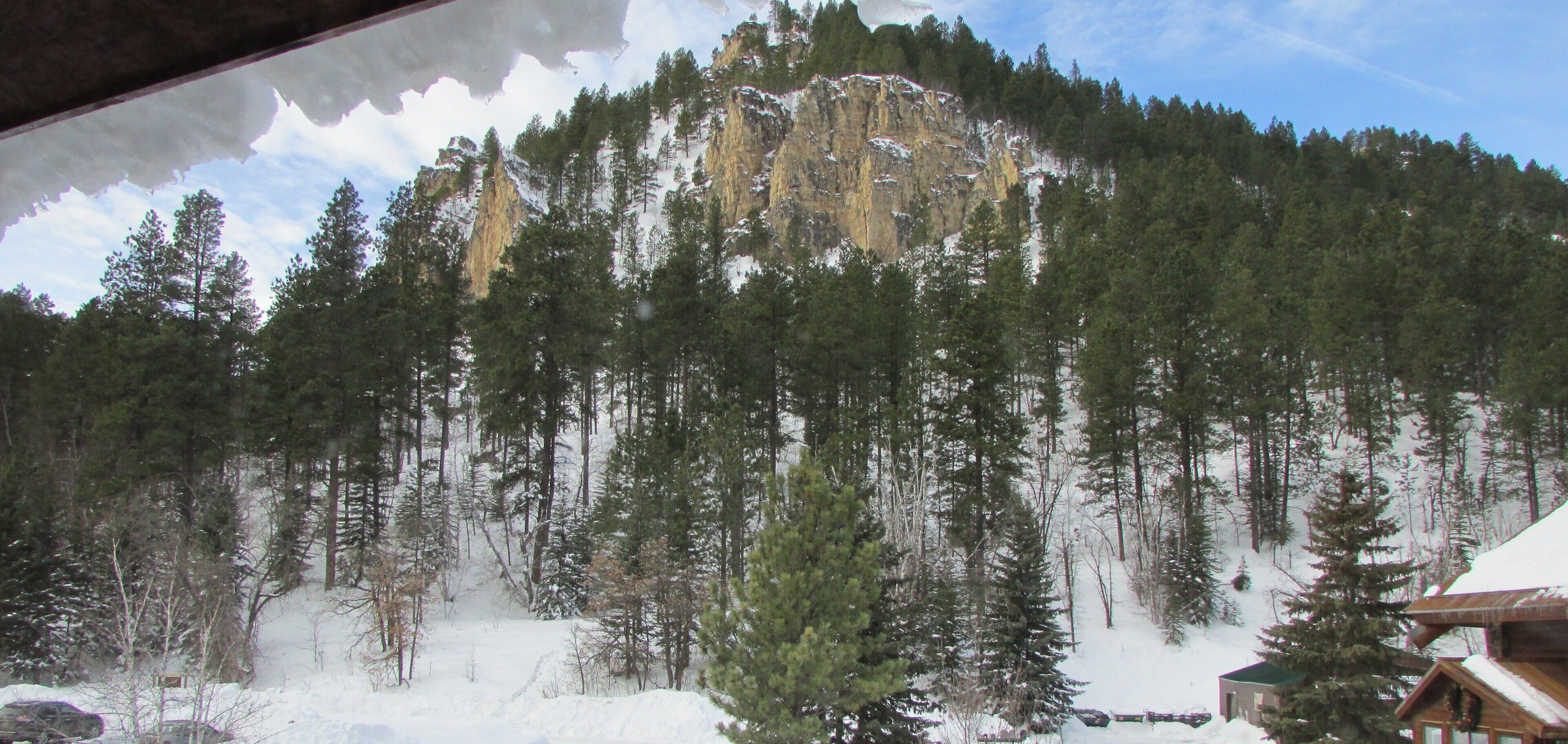 Paisaje montañoso con bosques densos y una cabaña en primer plano.