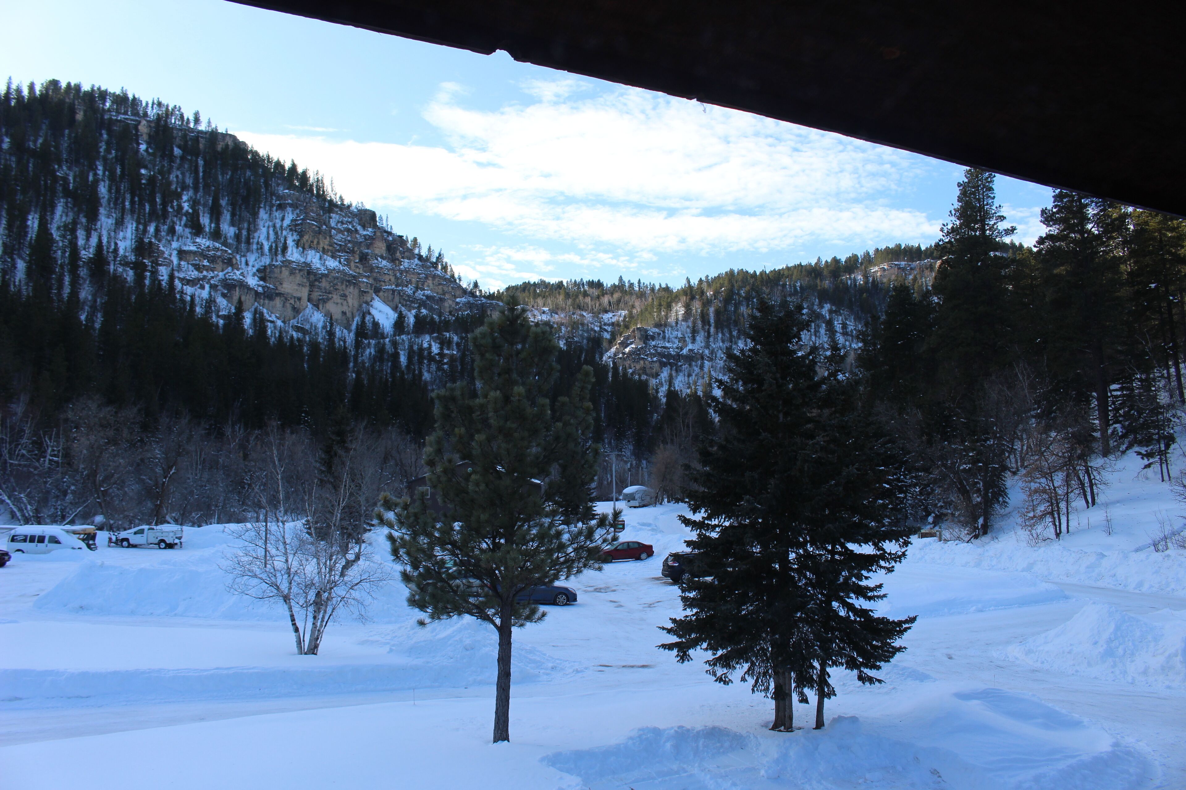 Un paysage enneigé avec une montagne, des arbres et des voitures garées.