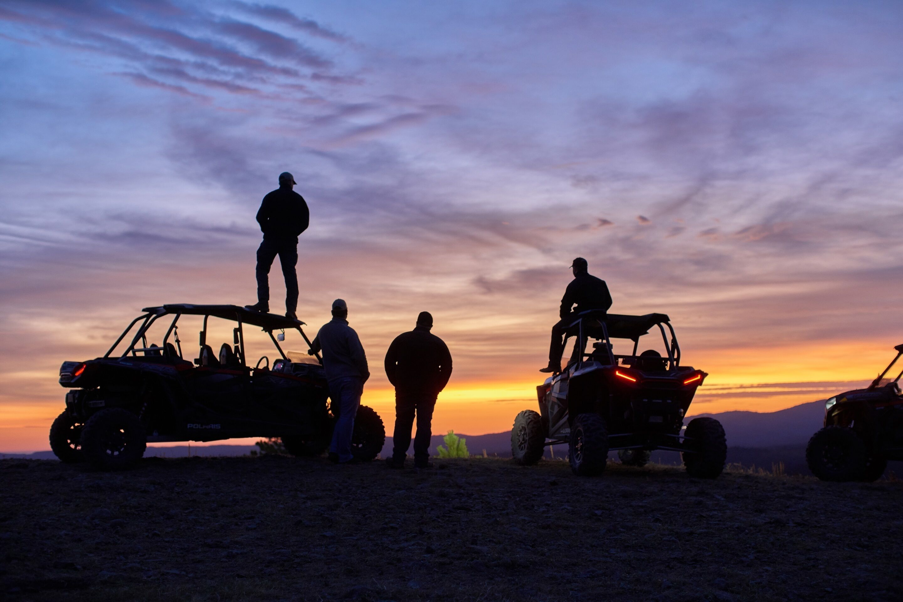 A group of people standing around off-road vehicles at sunset.