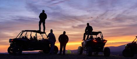 A group of people standing around off-road vehicles at sunset.