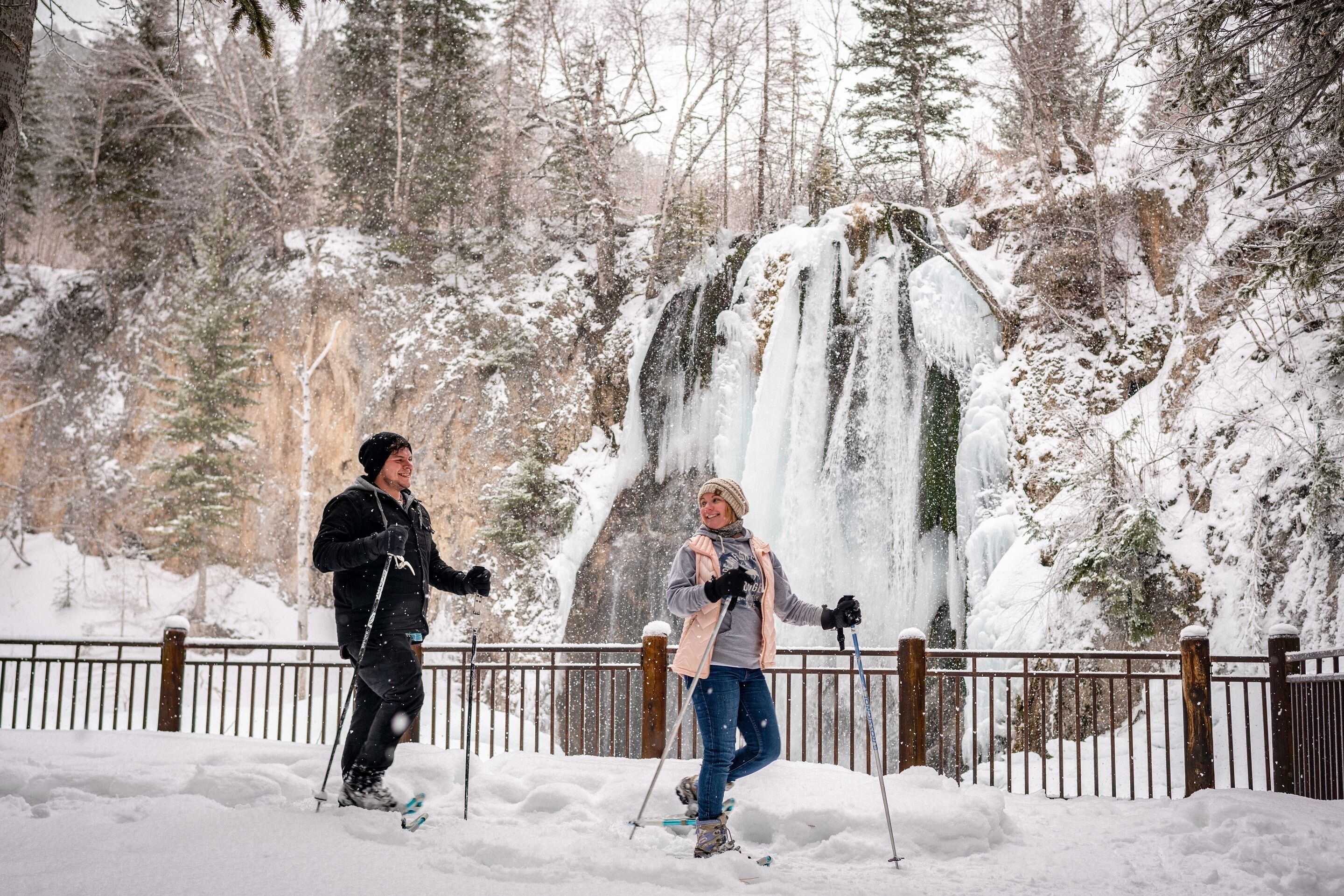 Schneebedeckte Landschaft mit einem Wasserfall und einem hölzernen Zaun.