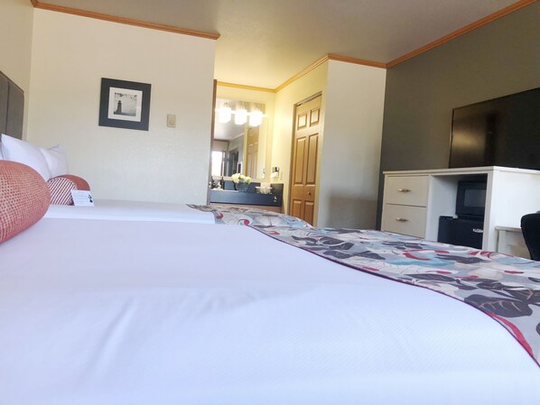 Habitación de hotel con dos camas, un escritorio, un espejo y una televisión.
