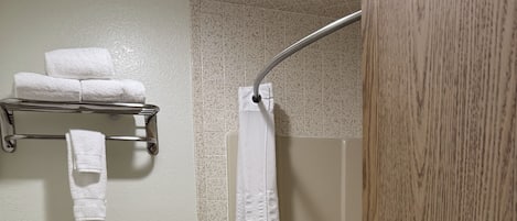 Un baño con inodoro, ducha con cortina, toallero y dispensador de papel higiénico.