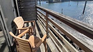 A wooden deck with two chairs and a table, overlooking a body of water with a bridge in the background.