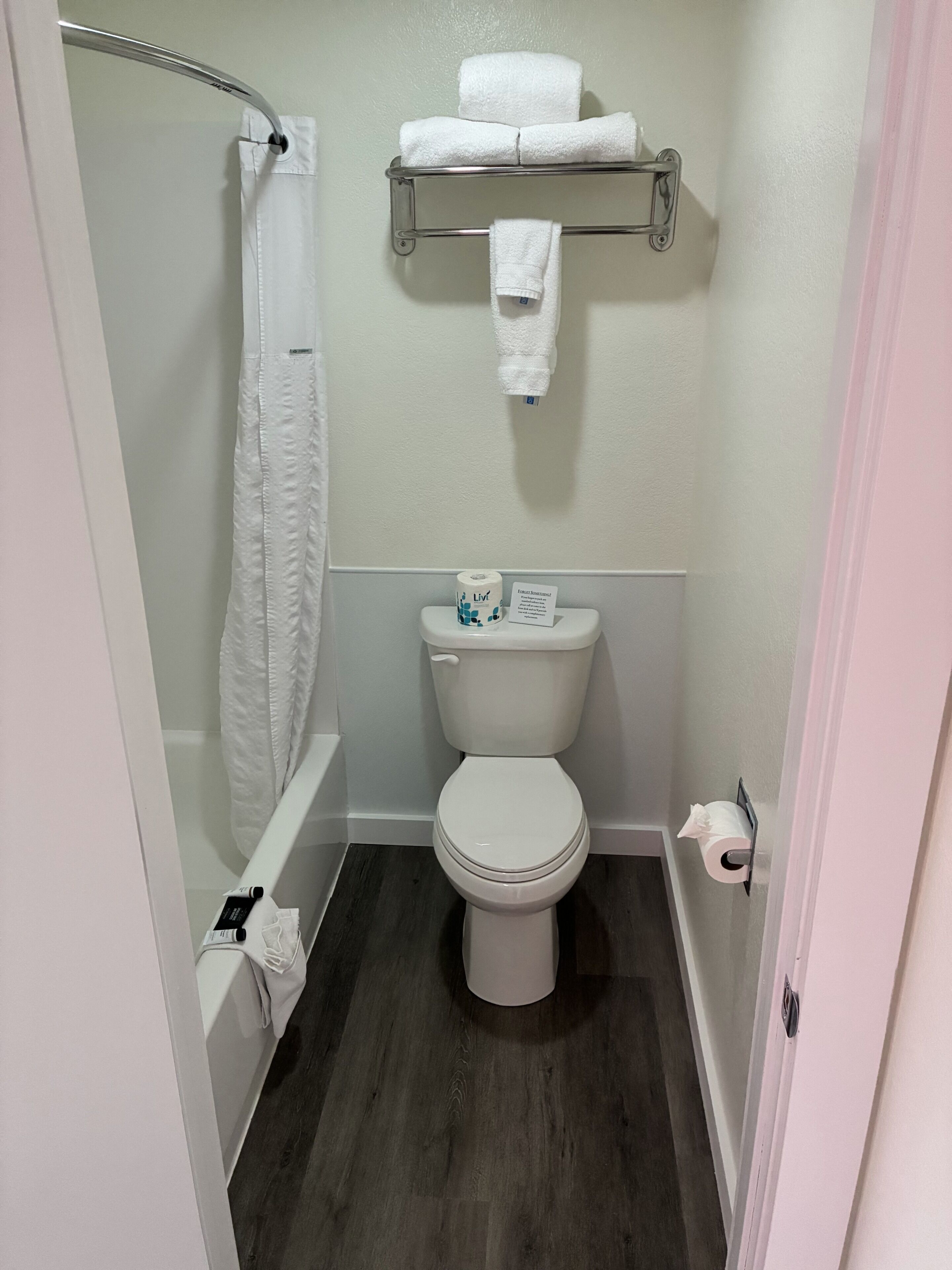 A bathroom with a toilet, a shower curtain, a towel rack with towels, and a toilet paper holder.