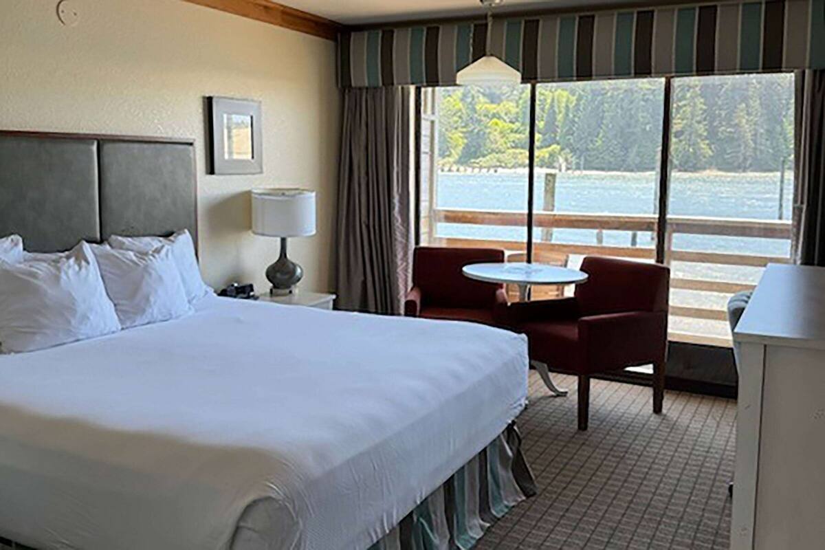 Ein Hotelzimmer mit einem großen Bett, einem Schreibtisch, einem Stuhl und Blick auf ein Gewässer durch das Fenster.