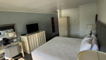 A hotel room with a large bed, a desk, a television, a wardrobe, and a lamp.