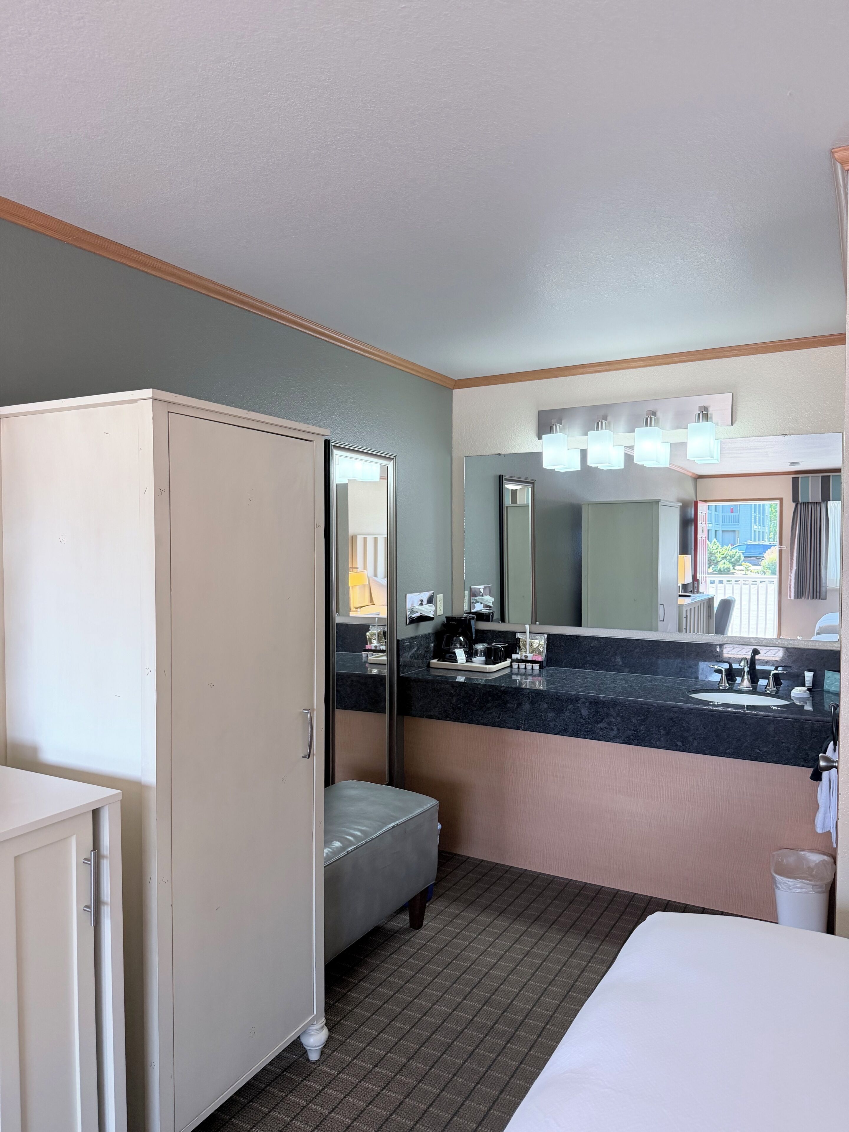 Une chambre d’hôtel comprenant un lit, une armoire, une coiffeuse avec un miroir, un lavabo et un petit coin salon.