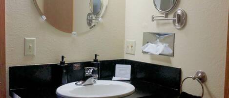 A bathroom with a round mirror, a rectangular mirror, and a sink with a black countertop. There are three wall-mounted lights above the mirrors.